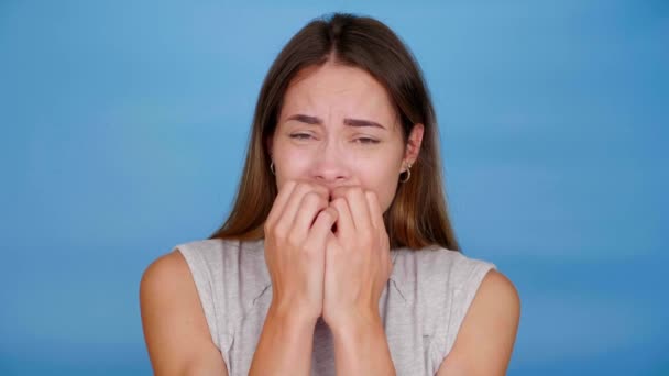 Mujer asustada en camiseta gris asustada, cierra los ojos con palmas sobre fondo azul — Vídeos de Stock