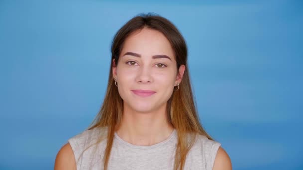 Mulher feliz bonita em cinza t-shirt olha câmera e sorrisos no fundo azul — Vídeo de Stock