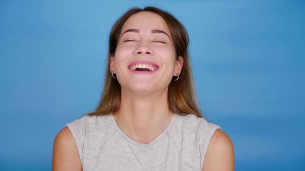 Hermosa mujer divertida en camiseta gris se ríe sobre fondo azul con espacio de copia — Vídeos de Stock