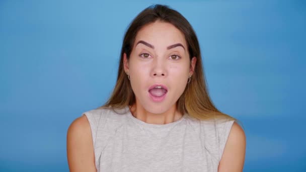 Beautiful woman in gray T-shirt shocked looking camera on blue background — Stock Video