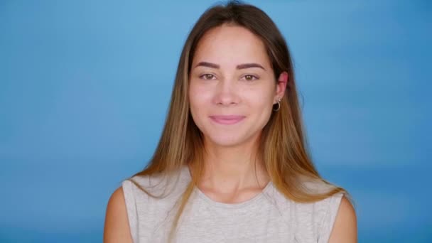 Mulher feliz em cinza t-shirt vira-se para a câmera e sorri no fundo azul — Vídeo de Stock