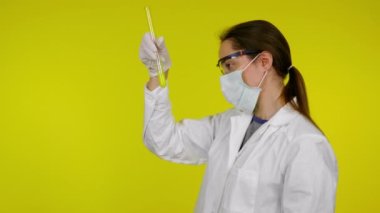Beyaz elbiseli kadın, koruyucu maske test tüpünün içindekileri inceliyor.
