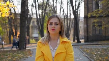 Pelerinli kadın, bluz duruyor, parktaki kameraya bakıyor, kamera kızı hareket ettiriyor.