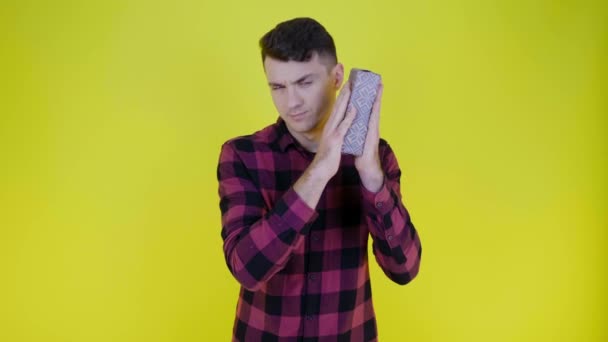 Nieuwsgierige man schudt doos met geschenk in de buurt van oor en probeert te begrijpen wat er in zit — Stockvideo