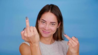 Gri tişörtlü kadın gülümsüyor, mavi arka planda orta parmağını gösteriyor.