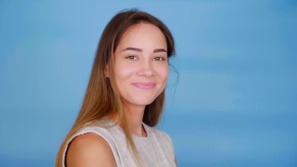 Happy woman in gray t-shirt turns to the camera and smiles on blue background — Stock Video