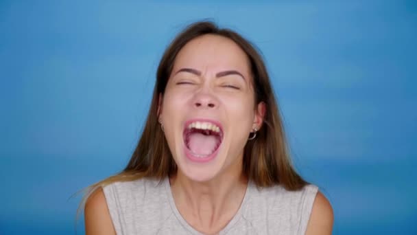 Vacker kvinna i grå t-shirt ropar på blå bakgrund med kopieringsutrymme — Stockvideo