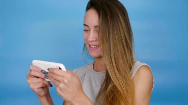 Emotionele positieve vrouw gamer speelt video game op smartphone, glimlacht, heeft plezier — Stockvideo