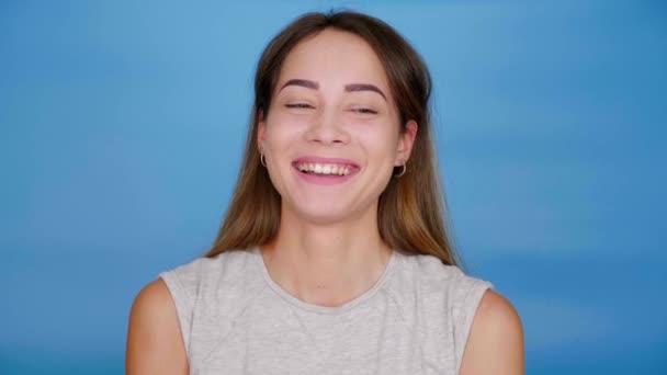 Schöne fröhliche Frau im grauen T-Shirt lacht auf blauem Hintergrund, Kopierraum — Stockvideo