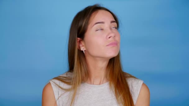 Beautiful woman in gray t-shirt looks around on blue background with copy space — Stock Video