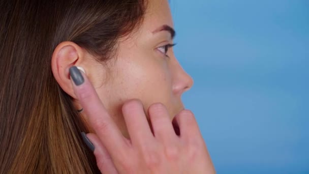 Close up head beautiful woman tap on wireless earphone in ear on blue background — Stock Video