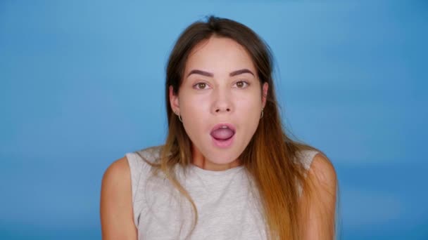 Chockad kvinna vänder sig till kameran på blå bakgrund med kopieringsutrymme — Stockvideo