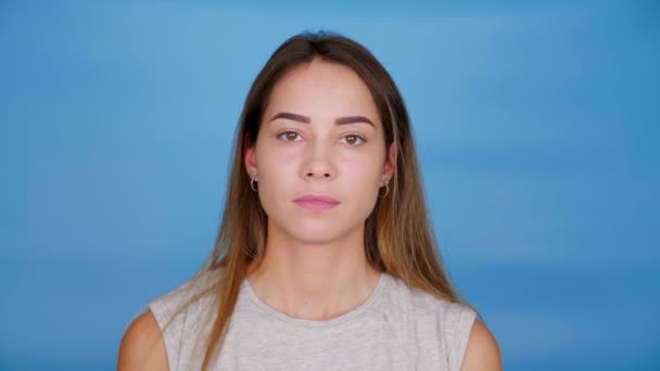 Woman in gray t-shirt looks camera on blue background with copy space — Stock Video