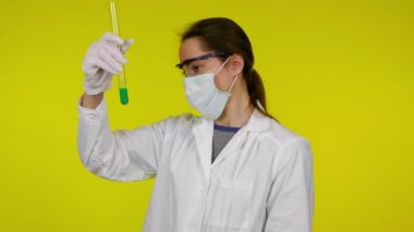 Koruyucu maskeli kadın test tüpünün içeriğini inceliyor ve hoşlanmadığını gösteriyor.