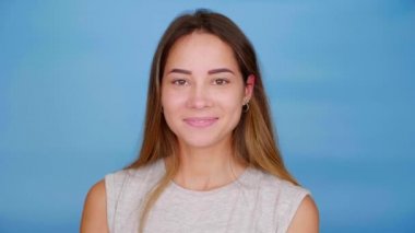 Gri tişörtlü mutlu kadın kameraya döner ve mavi arka planda gülümser.