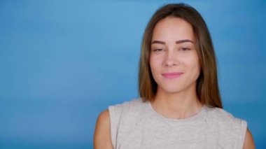 Gri tişörtlü güzel kadın gülümsüyor, elini kaldırıyor, mavi arka planda iyi görünüyor.