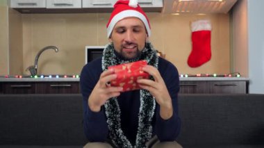 Kırmızı Noel Baba şapkalı adam, inceler, hediye kutusuyla öper, sarılır, gülümser.