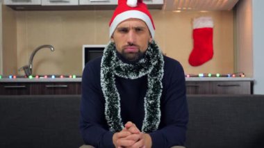 Yeni yılda kızgın bir adam. Kırmızı Noel Baba şapkası. Televizyon izliyor.