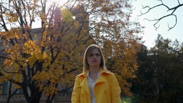 Vrouw in mantel, blouse staat, kijkt opzij tegen achtergrond boom met bladeren — Stockvideo