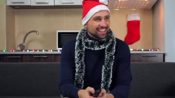 Vrolijke man in Nieuwjaar rode Kerstman hoed, kijkt weg, glimlachend — Stockvideo