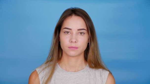 Žena v šedém tričku vypadá kamera na modrém pozadí s kopírovacím prostorem — Stock video
