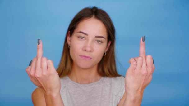 Positieve vrouw glimlacht, steekt handen op, toont middelvinger op blauwe achtergrond — Stockvideo