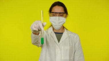 Beyaz elbiseli kadın, koruyucu maske test tüpünün içindekileri inceliyor.