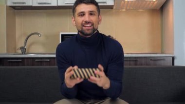 Mutlu yakışıklı adam çizgili kutuyu hediyeyle yakalar, inceler, gülümser ve kamerayı gösterir.