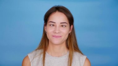 Gri tişörtlü, şaşı ve mavi arka planda gülümseyen güzel ve komik bir kadın.