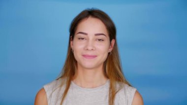Gri tişörtlü güzel mutlu kadın kameraya bakar ve mavi arka planda gülümser.