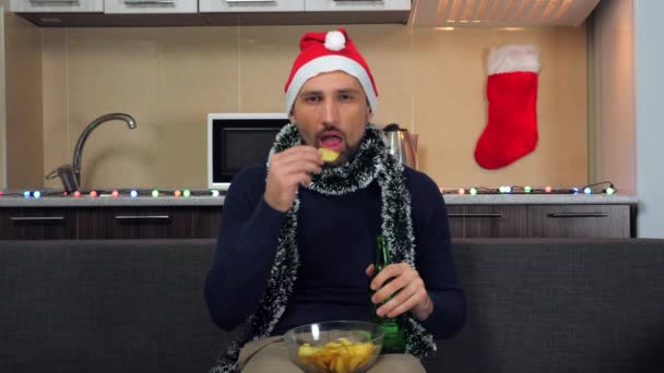 Hombre enfocado Año Nuevo Santa Claus sombrero come papas fritas, bebidas cerveza, viendo la televisión — Vídeos de Stock