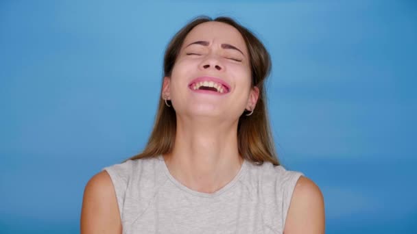 Belle femme gaie en gris T-shirt rit, regarde autour sur fond bleu — Video