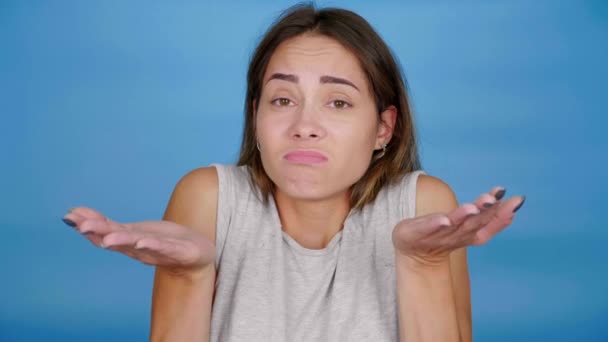 Não sei. Não sei. Mulher bonita em t-shirt encolhe os ombros, levanta as mãos no fundo azul — Vídeo de Stock