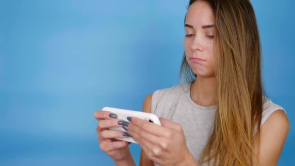 Beautiful female gamer plays video game on smartphone on blue background — Stock Video