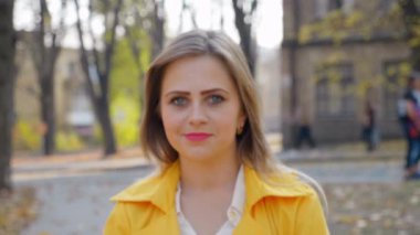 Kadın gülümsüyor, sonbahar parkında dikiliyor, kameraya bakıyor, kızı hareket ettiriyor.