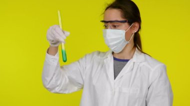 Koruyucu maskeli kadın test tüpünün içeriğini inceliyor, panikliyor ve elini sıkıyor.