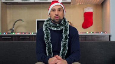Yeni yılda şok olmuş bir adam. Kırmızı Noel Baba şapkası. Televizyon izliyor, ağzını açıyor.