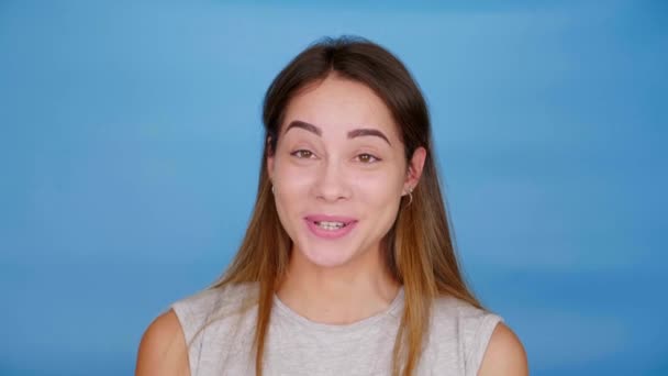 Vicces nő szürke pólóban beszél, hunyorog és mosolyog a kék háttér — Stock videók