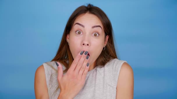 Wanita yang terkejut beralih ke kamera yang menutupi mulut dengan telapak tangan di latar belakang biru — Stok Video