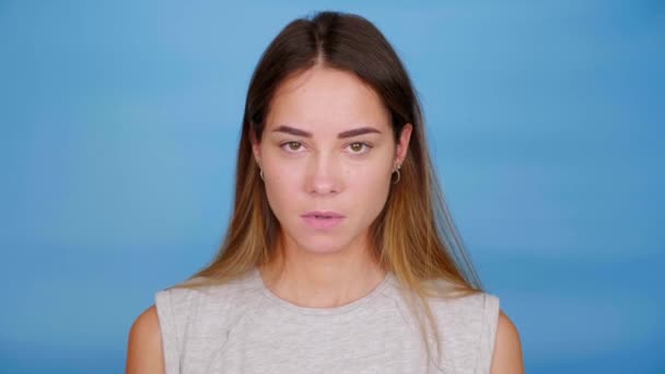Femme sérieuse émotionnelle en t-shirt gris montre majeur sur fond bleu — Video