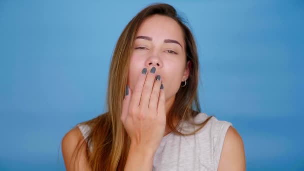 Schöne Frau im grauen T-Shirt schickt einen Luftkuss auf blauem Hintergrund — Stockvideo