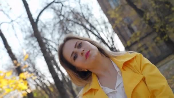 Femme en manteau jaune, blouse se tient dans le parc d'automne, regarde la caméra tourne — Video