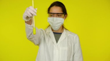 Beyaz elbiseli kadın, koruyucu maske test tüpünün içindekileri inceliyor.