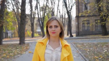 Sarı pelerinli, bluzlu mutlu kadın gülümseyen, ayakta duran, parkta kameraya bakan.