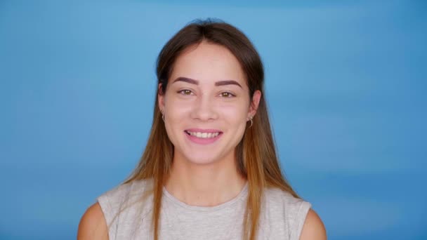 Mooie grappige vrouw in grijs T-shirt squints en lacht op blauwe achtergrond — Stockvideo