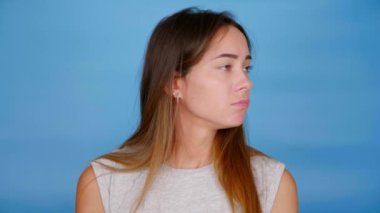 Üzgün kadın etrafına bakıyor, elini kaldırıyor mavi arka planda seçim yapamıyor.