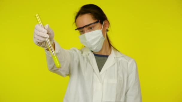 Vrouw in witte medische jurk, beschermend masker is onderzoekt de inhoud van de reageerbuis — Stockvideo