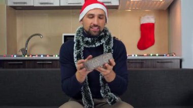 Kırmızı Noel Baba şapkalı adam, kar taneleriyle kutu yakalar, inceler, gülümser.