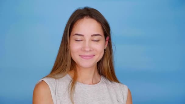 Femme heureuse en t-shirt gris se tourne vers la caméra et sourit sur fond bleu — Video