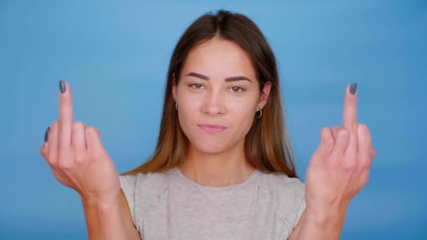 Позитивная женщина улыбается, поднимает руки, показывает средний палец на синем фоне — стоковое видео